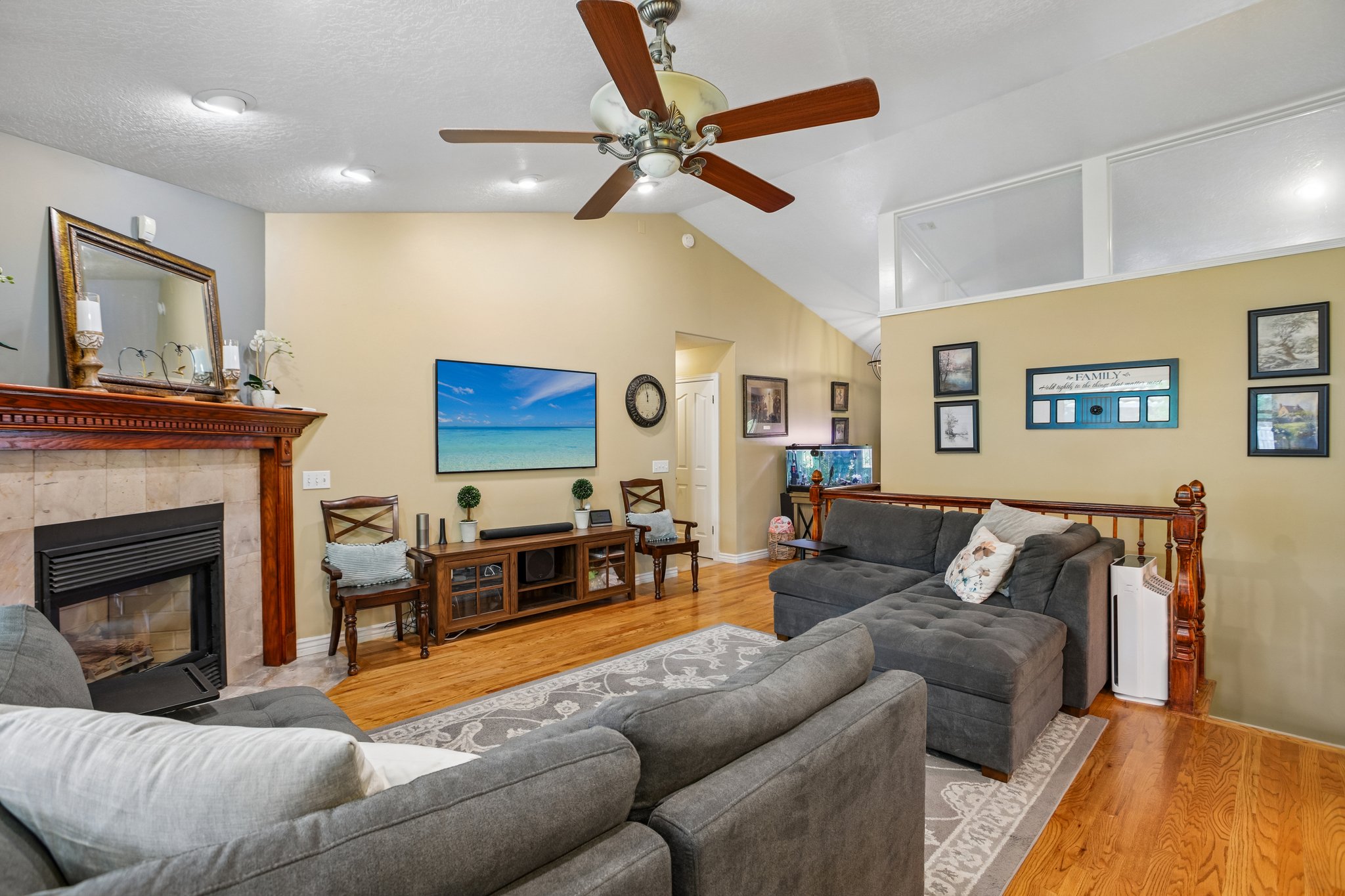 Living room featuring light wood-style flooring, lofted ceiling, a ceiling fan, and a tiled fireplace