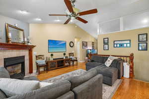 Living room featuring light wood-style flooring, lofted ceiling, a ceiling fan, and a tiled fireplace