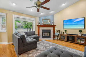 Living area featuring lofted ceiling, light wood-style floors, a fireplace, and a ceiling fan