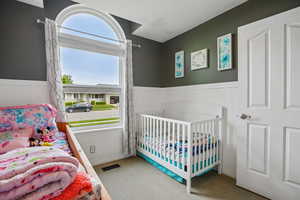 Bedroom with wainscoting, a nursery area, light colored carpet, and wood walls