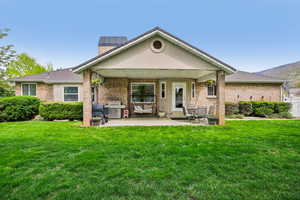 Back of property featuring a yard, brick siding, a patio area, and a chimney