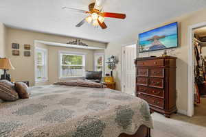 Bedroom featuring a walk in closet, a textured ceiling, light colored carpet, and a ceiling fan