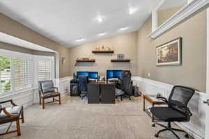 Home office featuring a decorative wall, wainscoting, vaulted ceiling, and light carpet