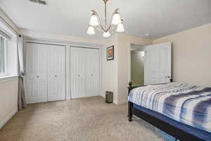 Bedroom with two closets, light carpet, a chandelier, and a textured ceiling
