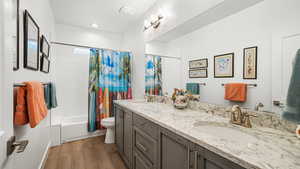 Bathroom with double vanity, shower / bathtub combination with curtain, and light wood-style flooring