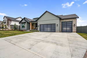 View of front of property featuring board and batten siding, an attached garage, concrete driveway, stone siding, and covered porch