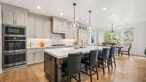 Kitchen with a breakfast bar area, light wood-style flooring, a center island with sink, stainless steel appliances, and tasteful backsplash