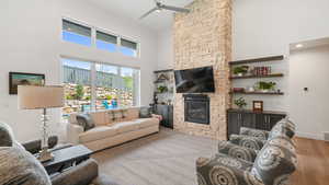 Living room with a high ceiling, a stone fireplace, a ceiling fan, and carpet floors