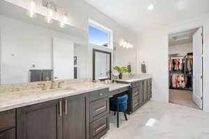 Full bathroom featuring two vanities, a walk in closet, and light marble finish floors
