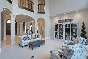 Living room featuring arched walkways, decorative columns, light carpet, a high ceiling, and recessed lighting
