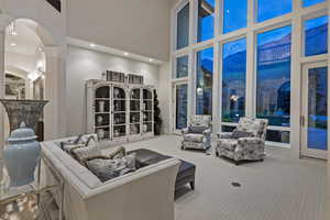 Carpeted living area with a high ceiling, arched walkways, ornate columns, recessed lighting, and expansive windows