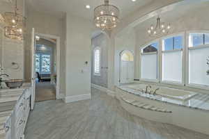 Ensuite bathroom with a chandelier, vanity, a garden tub, and healthy amount of natural light