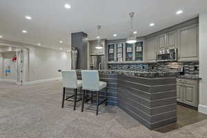 Kitchen with gray cabinets, a breakfast bar, a kitchen island with sink, stainless steel appliances, and tasteful backsplash
