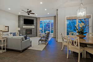 Living room featuring dark wood-style flooring, a fireplace, a ceiling fan, and suspended lighting