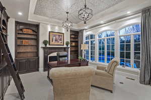 Carpeted living area with a chandelier, an office area, built in shelves, and a tray ceiling