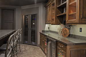Kitchen featuring beverage cooler, dark stone counters, glass insert cabinets, and dark wood finish cabinetry