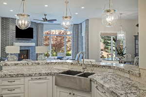 Kitchen with ceiling fan, light stone countertops, white cabinetry, a tiled fireplace, and open floor plan