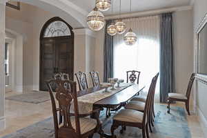 Dining area with arched walkways, suspended lighting, ornamental molding, and stone tile floors