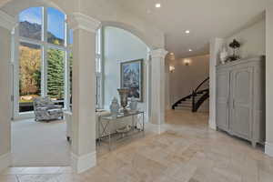 Hall featuring arched walkways, ornate columns, light colored carpet, stone tile flooring, and a high ceiling