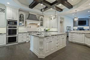 Kitchen featuring dark wood finished floors, stainless steel appliances, glass fronted cabinets, white cabinetry, and coffered ceiling