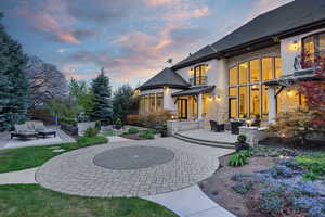 Back of property at dusk with an outdoor lounge area, a patio area, stucco siding, a shingled roof, and stone siding