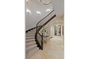 Stairway featuring arched walkways, a chandelier, stone finish flooring, and a high ceiling