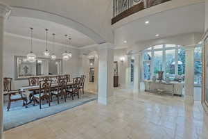 Dining area with ornate columns, stone tile floors, crown molding, hanging lights, and arched walkways