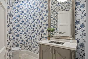 Half bath featuring wallpapered walls, vanity, and light tile patterned floors