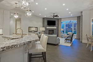 Kitchen with light stone counters, dark wood finished floors, a kitchen breakfast bar, pendant lighting, and a fireplace