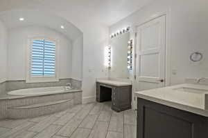 Bathroom with a bath, two vanities, recessed lighting, and lofted ceiling