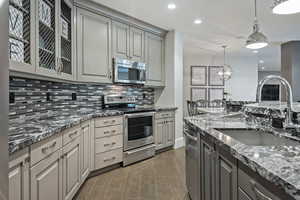 Dual tone kitchen with stainless steel appliances, dark stone countertops, wood tiled floors, glass fronted cabinets, and dual tone cabinets