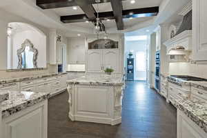 Kitchen with decorative backsplash, coffered ceiling, dark wood-type flooring, light stone counters, and a kitchen island