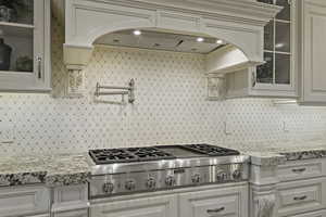 Kitchen featuring glass fronted cabinets, stainless steel gas cooktop, light stone counters, and backsplash