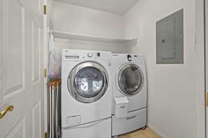 Laundry area featuring electric panel, washer and clothes dryer, and light tile patterned floors