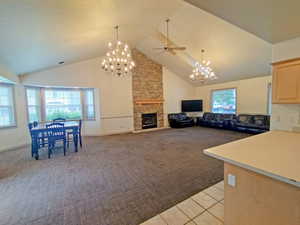 Living area with light carpet, a high ceiling, ceiling fan, a chandelier, and a fireplace