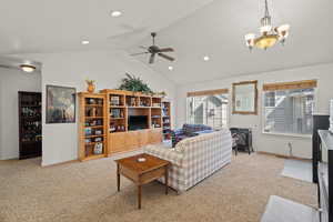 Living area featuring ceiling fan, light carpet, a wood stove, hanging lights, and a high ceiling
