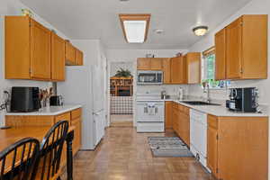 Kitchen featuring white appliances, light countertops, wood finish cabinets, brick patterned flooring, and a textured ceiling