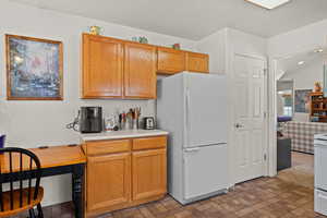 Kitchen featuring white appliances, light countertops, brick patterned floors, built in study area, and wood finish cabinetry