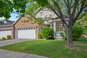 View of front of home with an attached garage, concrete driveway, a front lawn, and brick siding