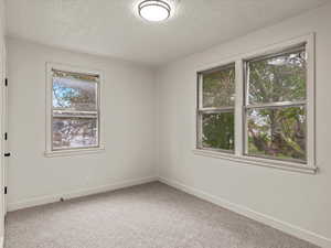 Empty room with light colored carpet and a textured ceiling