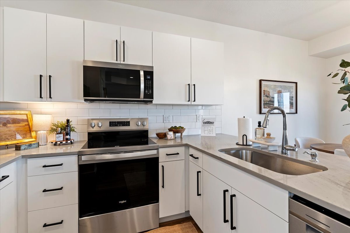 Kitchen featuring stainless steel appliances, white cabinets, light stone counters, and tasteful backsplash