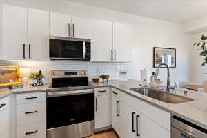 Kitchen featuring stainless steel appliances, white cabinets, light stone counters, and tasteful backsplash