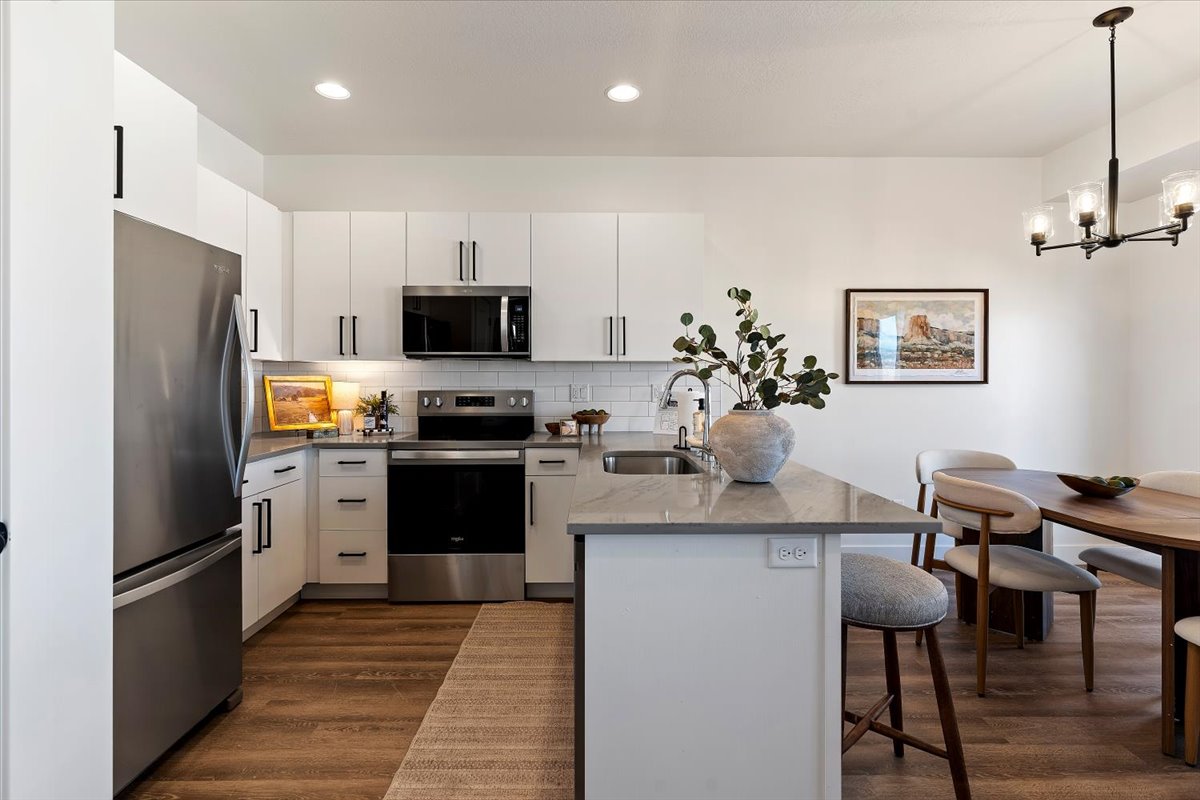 Kitchen featuring a peninsula, stainless steel appliances, white cabinetry, dark wood-style flooring, and a kitchen bar
