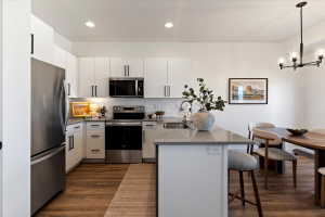 Kitchen featuring a peninsula, stainless steel appliances, white cabinetry, dark wood-style flooring, and a kitchen bar
