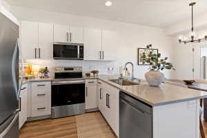 Kitchen featuring stainless steel appliances, light stone countertops, a peninsula, and white cabinetry