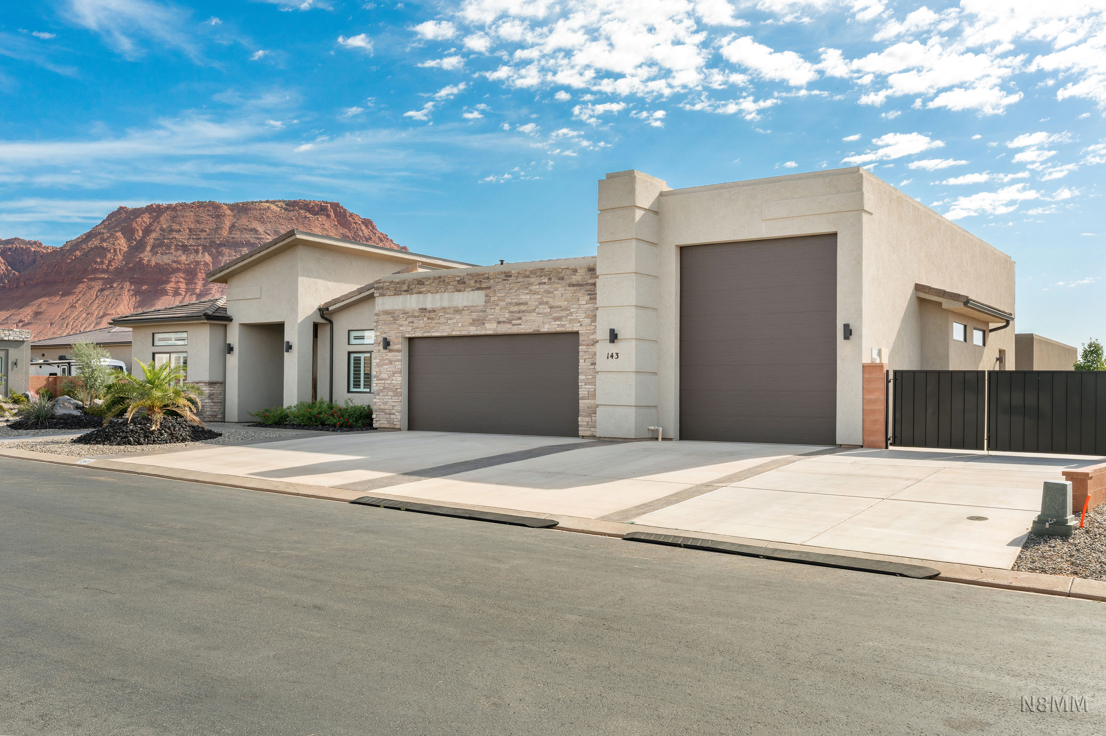View of front facade featuring a garage, stucco siding, stone siding, and driveway