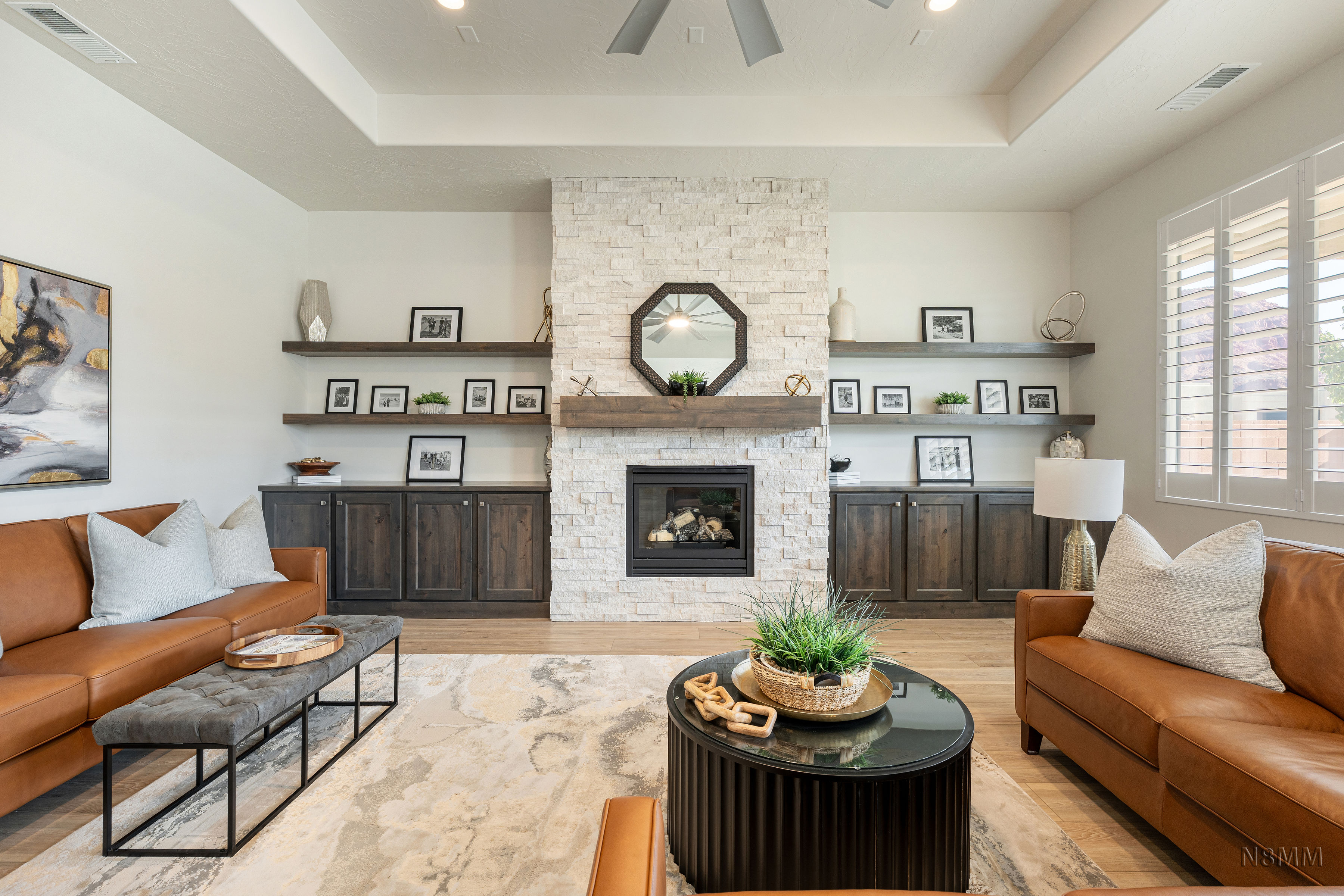 Living room with a tray ceiling, light wood-style flooring, a stone fireplace, and ceiling fan