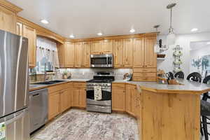 Kitchen with a kitchen breakfast bar, a peninsula, stainless steel appliances, hanging light fixtures, and light countertops