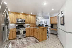 Kitchen with a breakfast bar area, stainless steel appliances, a peninsula, decorative light fixtures, and light tile patterned floors