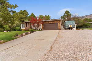 Ranch-style house with concrete driveway, an attached garage, a chimney, a front yard, and stone siding